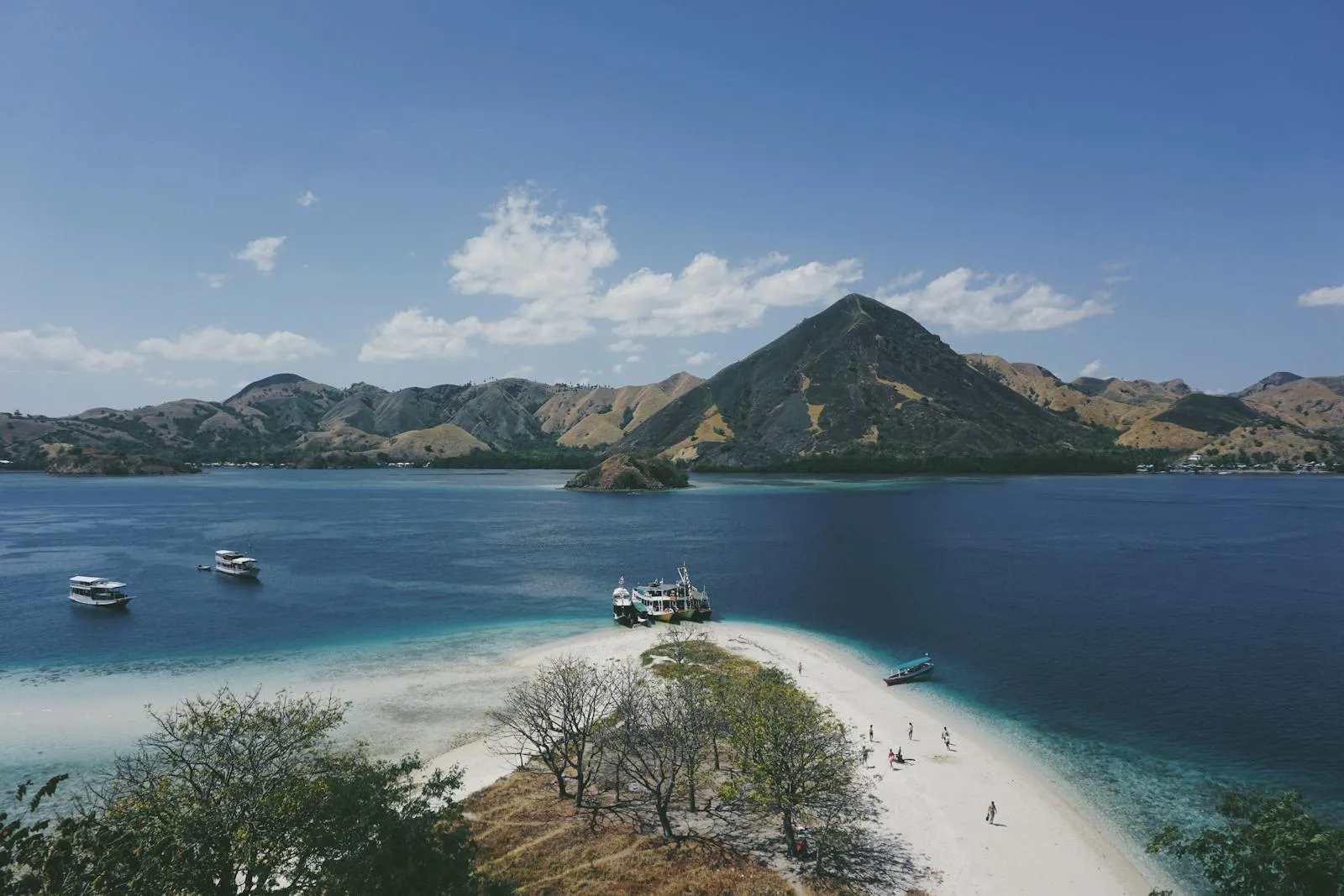 Stunning aerial view of Komodo Island's coastline with turquoise waters and distant mountains under a clear blue sky.