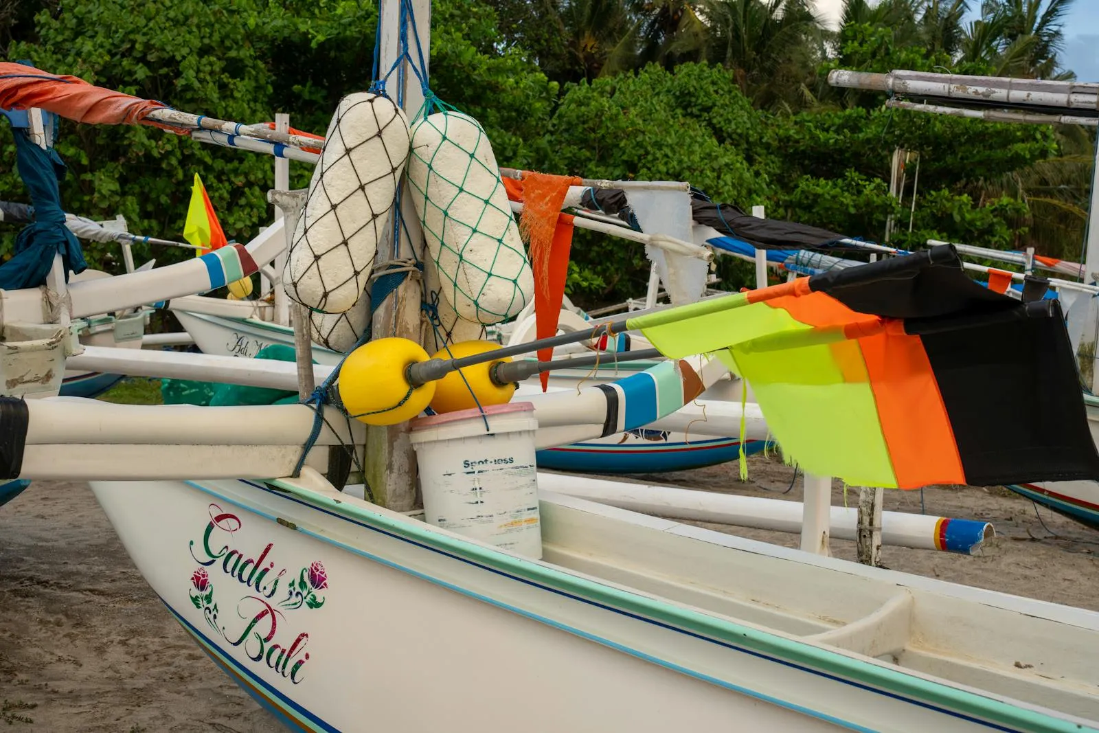 Colorful traditional fishing boats with flags on a sandy Bali beach.