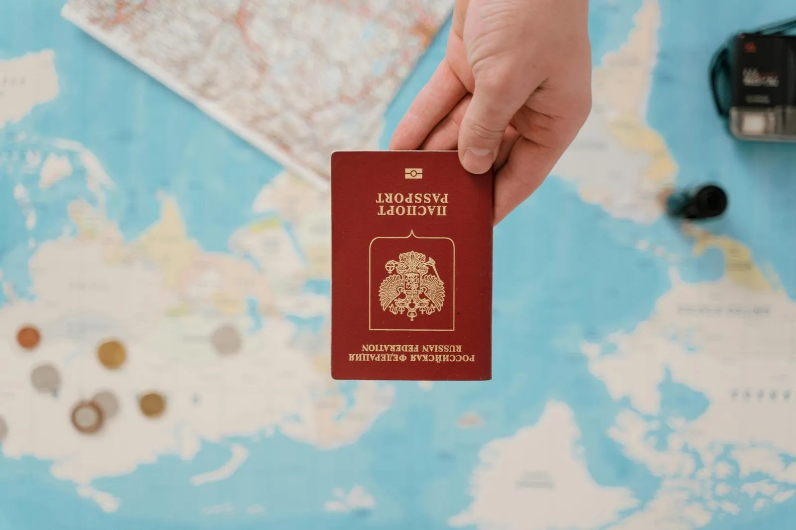 A hand holding a Russian passport above a travel-themed map, capturing world travel concepts.