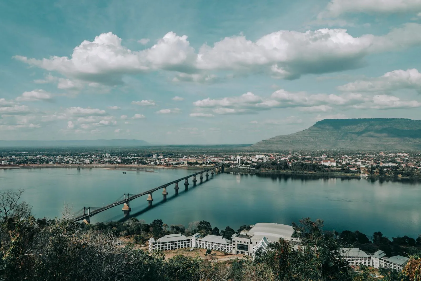 A picturesque bridge spans the Mekong River in a tranquil Laotian landscape.