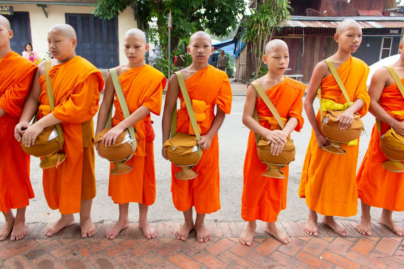 Buddhist monks in vibrant robes walking outdoors, holding alms bowls during a spiritual procession.