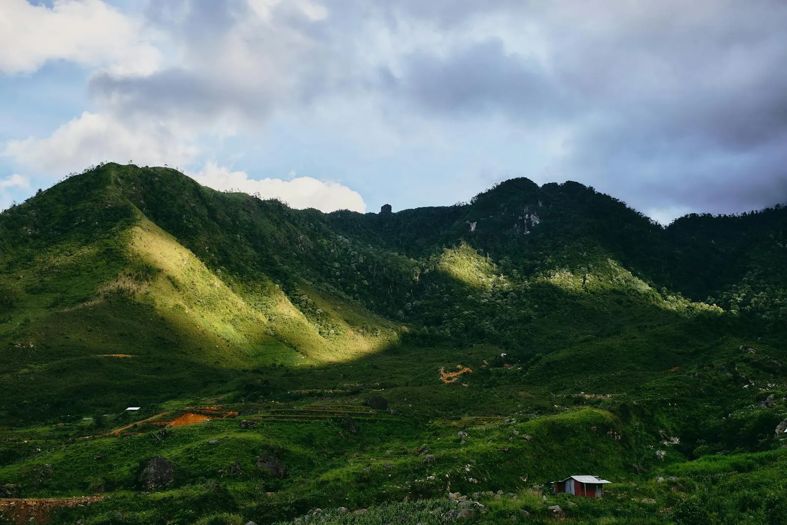 Breathtaking aerial view of lush green hills and valleys in L?o Cai, Vietnam, under a cloudy blue sky.