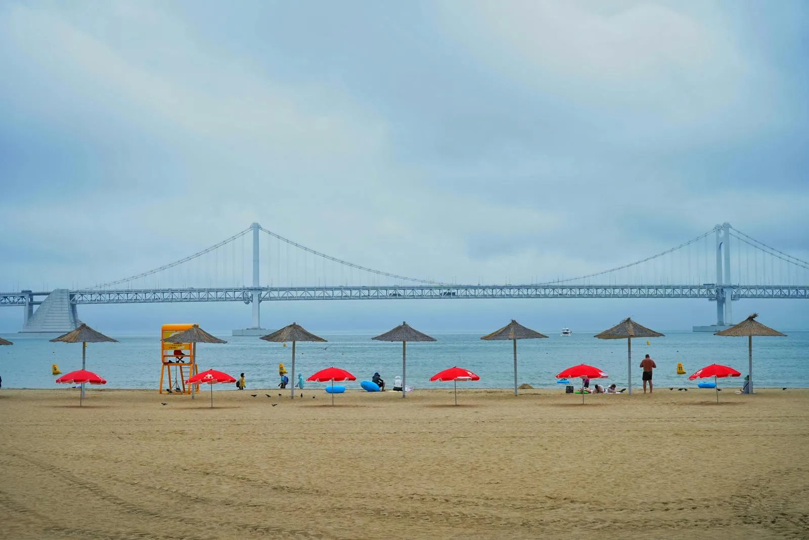 Relaxing beach scene featuring Gwangan Bridge in Korea with umbrellas and a lifeguard stand.