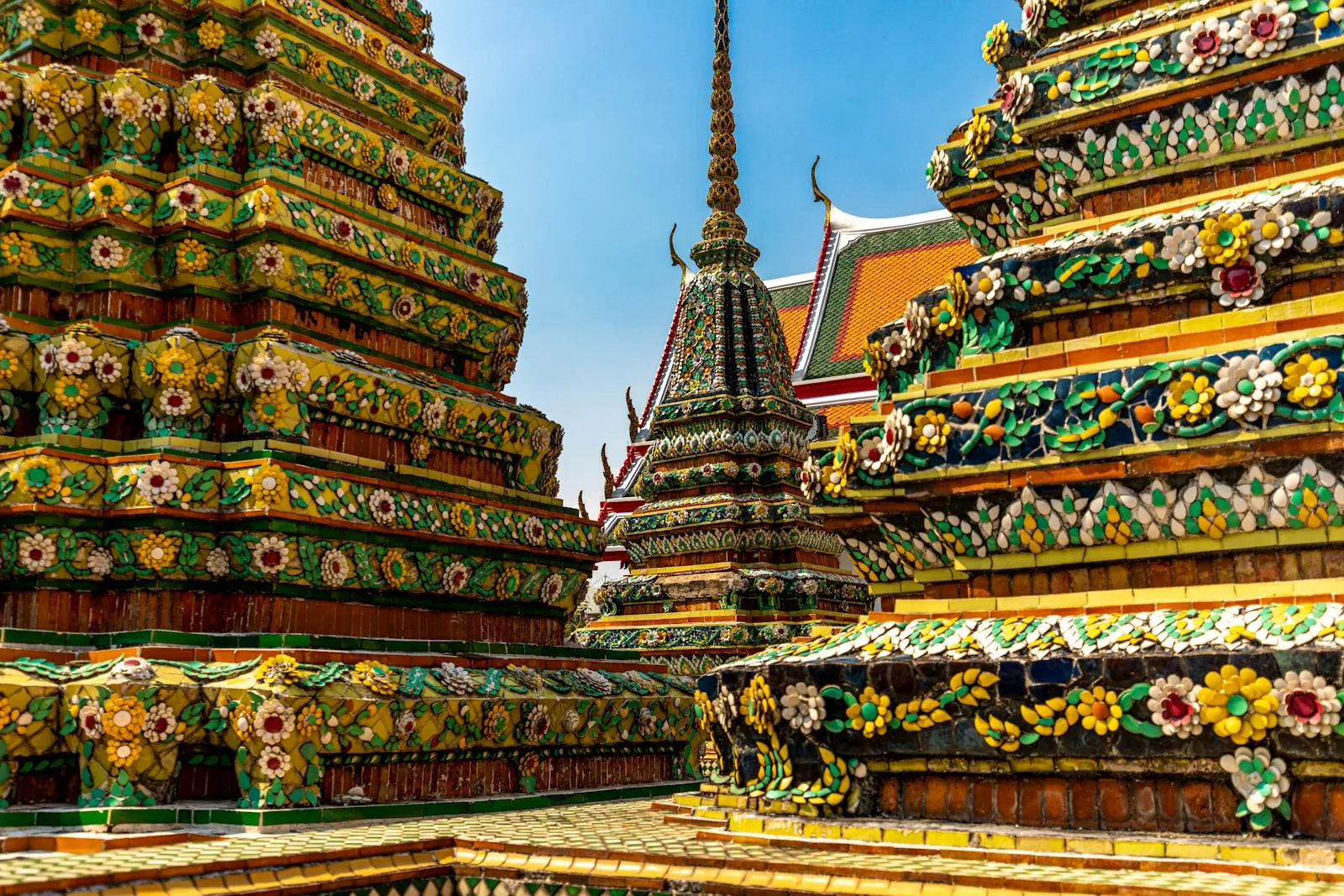 Colorful and ornate temples of Wat Pho in Bangkok, showcasing intricate Thai architecture under a clear blue sky.