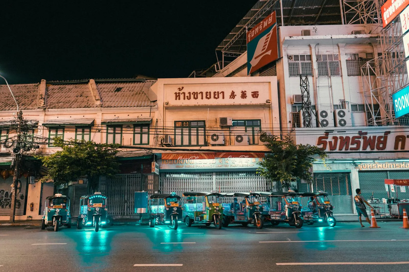 Vibrant night scene featuring electric tuk-tuks parked in front of lit-up city buildings.