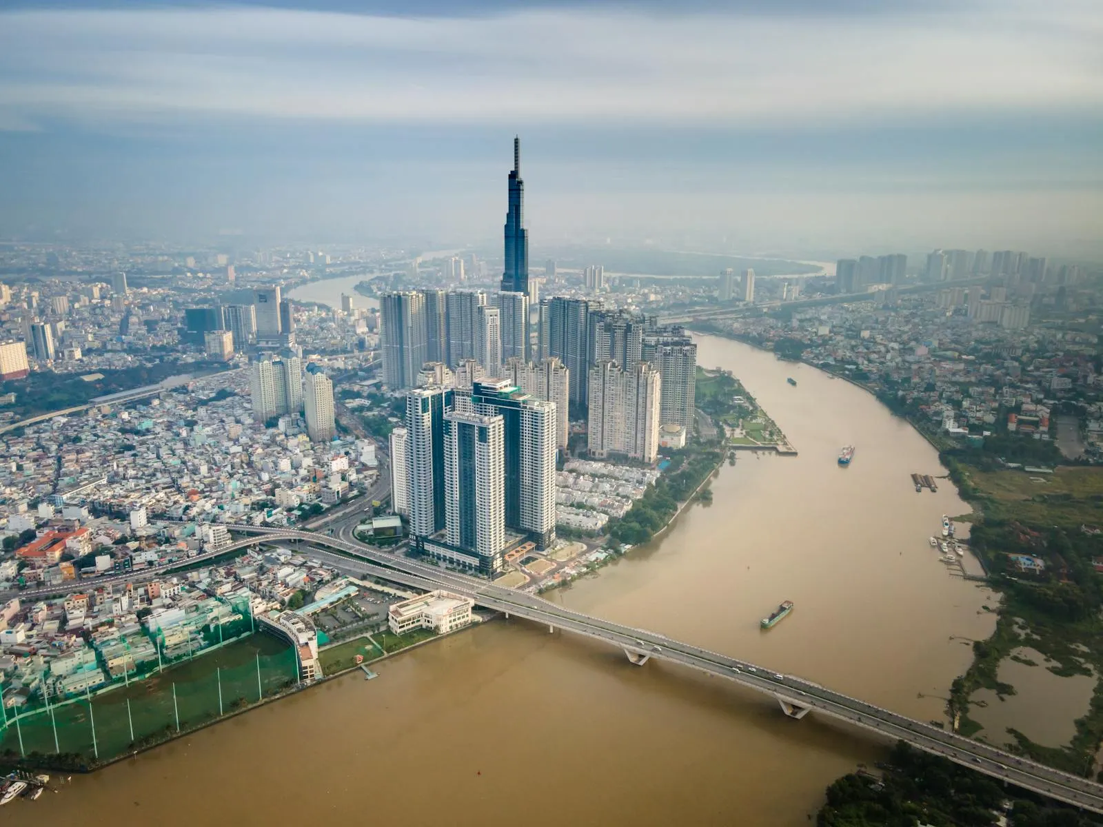 Aerial perspective of Ho Chi Minh City's modern skyline with river and bridge.